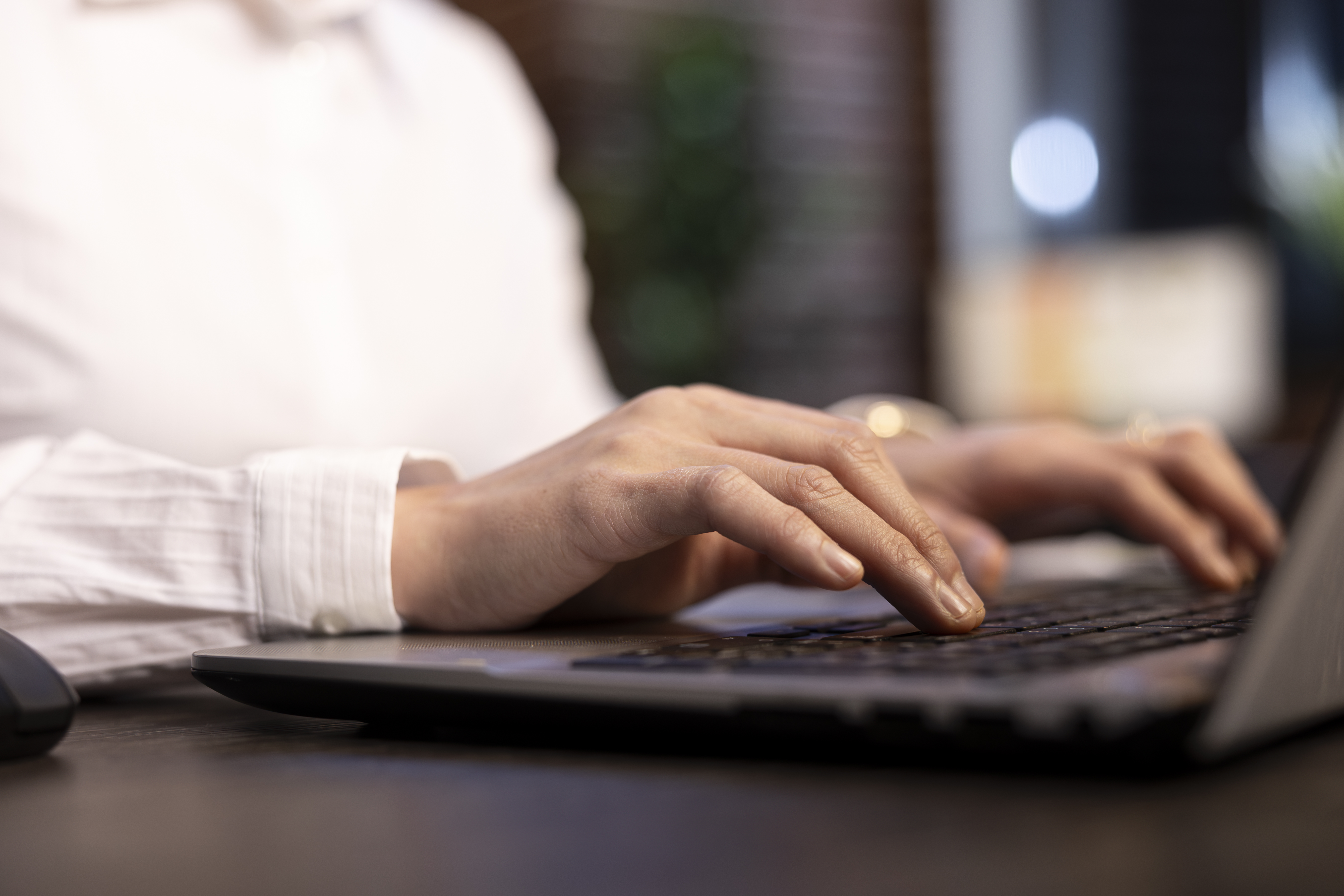Close up of a person typing on a laptop, wearing a long sleeved white shirt